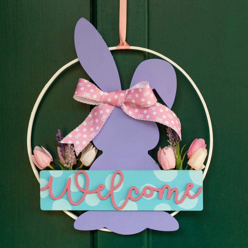 Decorative Easter sign with a bunny silhouette, pink bow, and 'Welcome' text on a green background.