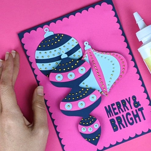 Handmade Christmas card with decorative baubles and 'Merry & Bright' text on a pink background.