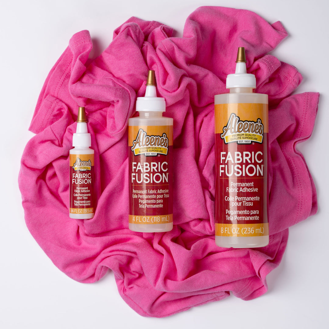 Three bottles of Aleene's Fabric Fusion on a pink fabric background