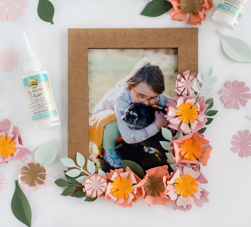 Decorative photo frame with flowers and a bottle of glue on a white background