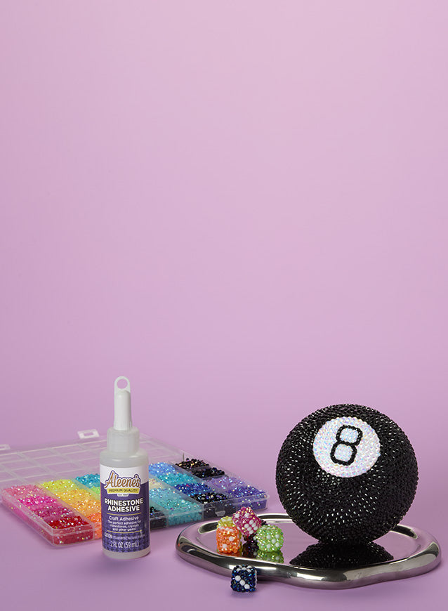 
Decorative eight-ball with rhinestones, Aleene's adhesive, and rhinestone tools on a pink background